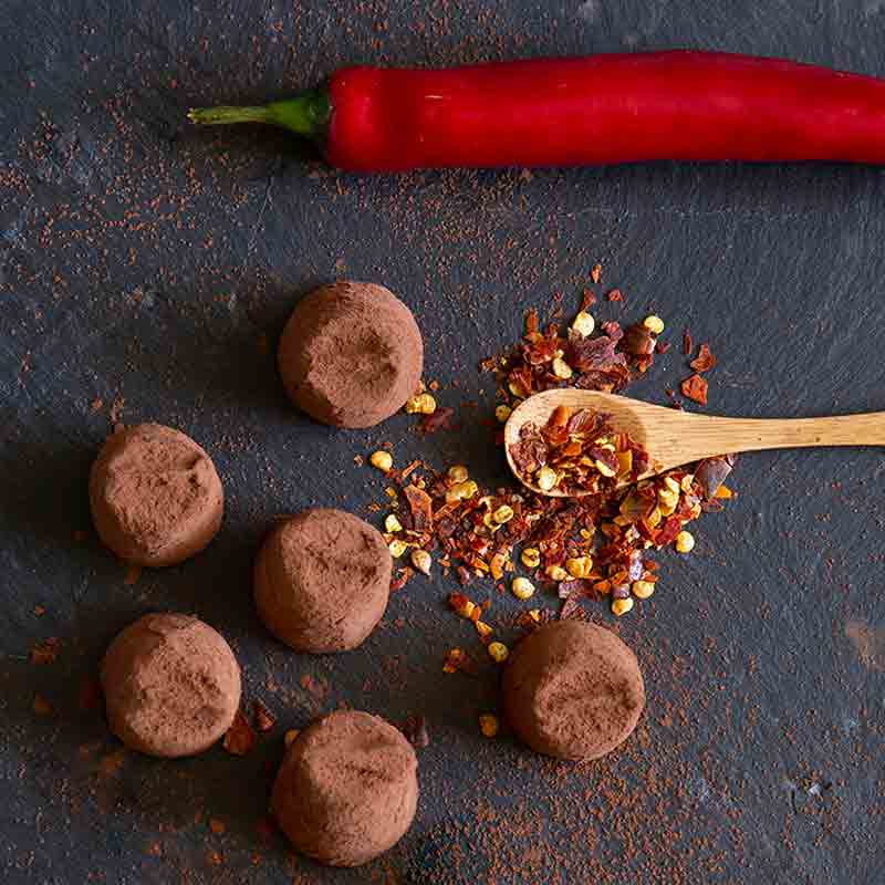 Schokoladentrüffel, Chilischote, Chiliflocken auf dunklem Untergrund.