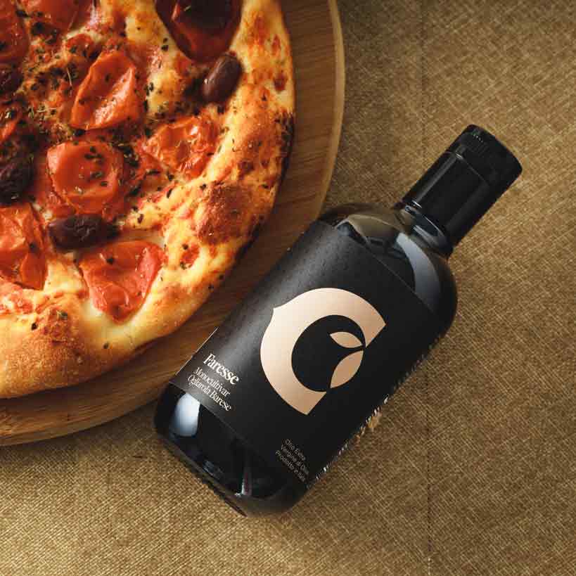 Flasche Olivenöl "Foresse" neben Pizza auf Tisch.