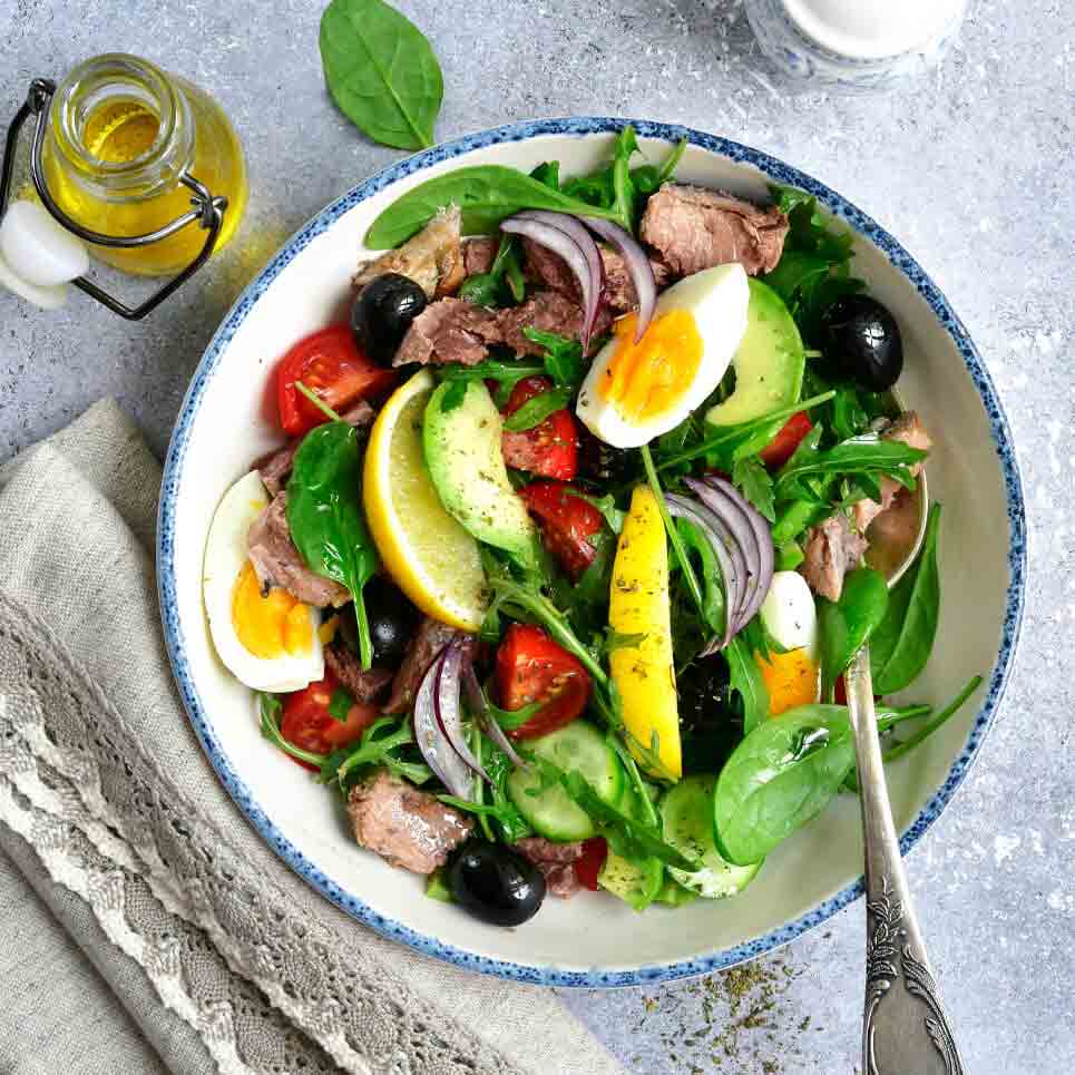 Salat mit Thunfisch, Eiern, Oliven, Dressing und Gemüse.