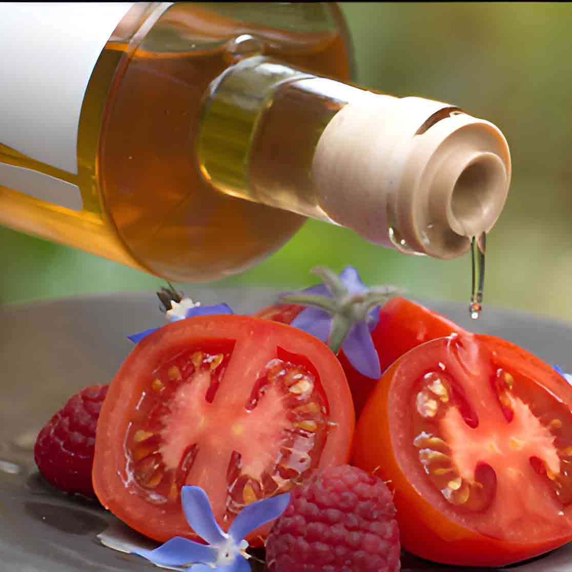 Flasche Essig über Tomaten, Himbeeren und blauen Blüten.