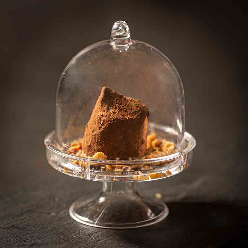 Praline unter Glasglocke auf schwarzem Hintergrund, dekorativ präsentiert.