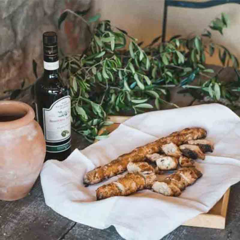Olivenölflasche, Brot, Tonkrug, Olivenzweige auf Holztisch.
