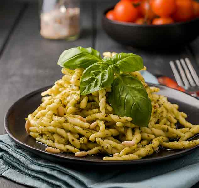Teller mit Trofie-Pasta, Pesto und Basilikumblättern.