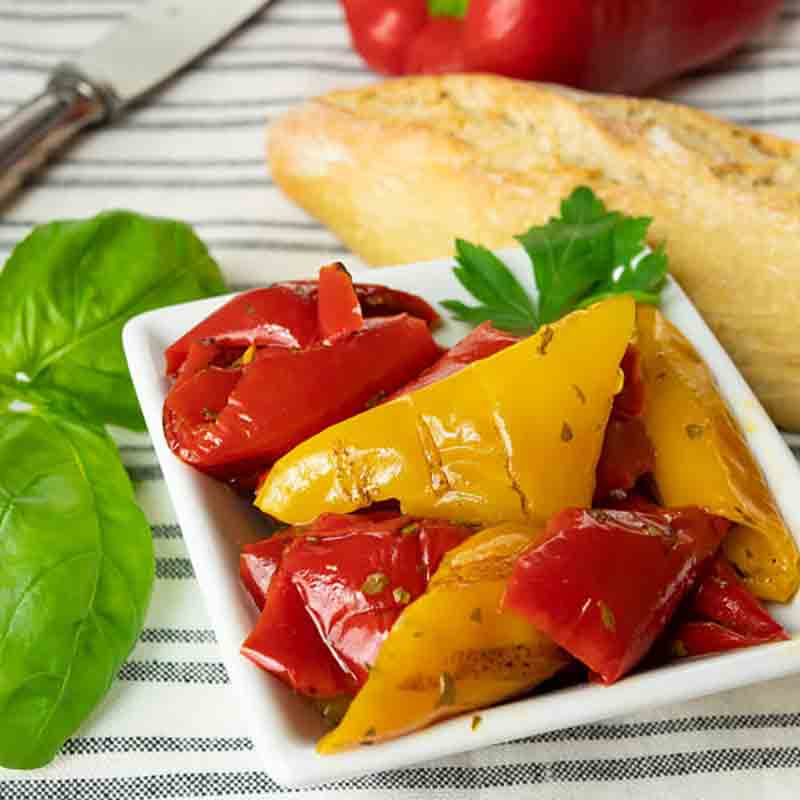Gegrillte Paprika, Baguette, Basilikum, Petersilie auf gestreiftem Tuch.