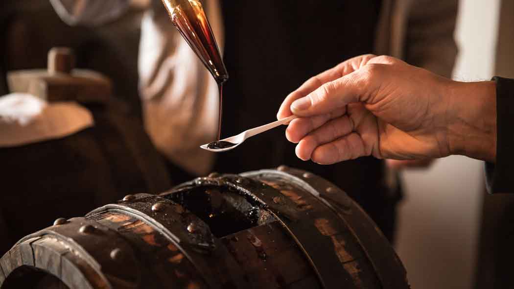 Hand hält Löffel unter Balsamico-Fass-Auslauf.