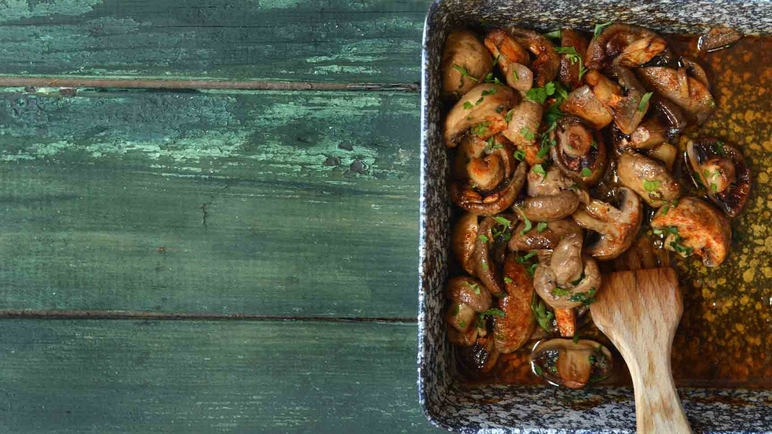 Pilze in Balsamico-Marinade auf grünem Holztisch.