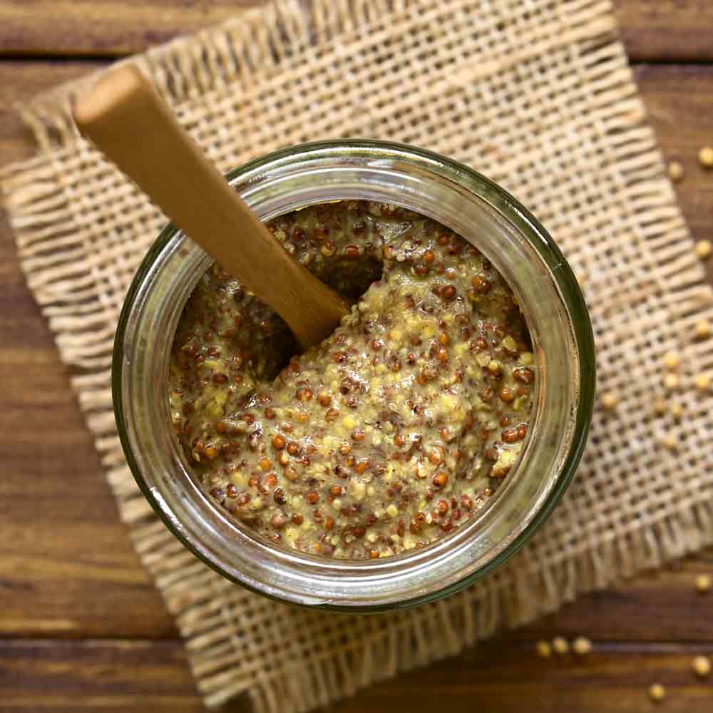 Glas Dijon-Senf mit Holzlöffel auf Juteunterlage.