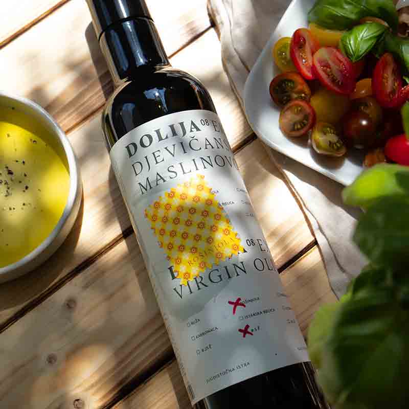 Dolija Olivenölflasche neben Tomaten und Basilikum.