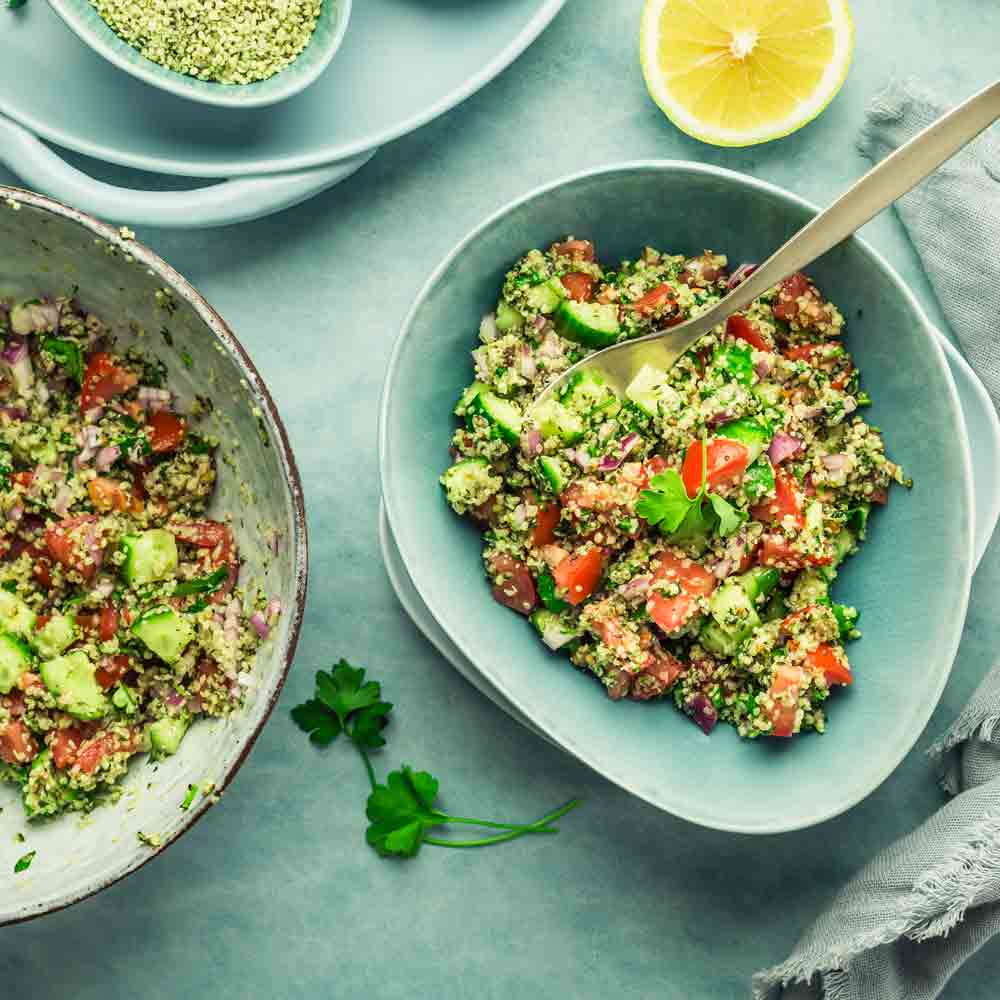Tabouleh-Salat mit Hanfsamen, Gemüse und Zitronenscheibe auf Teller.