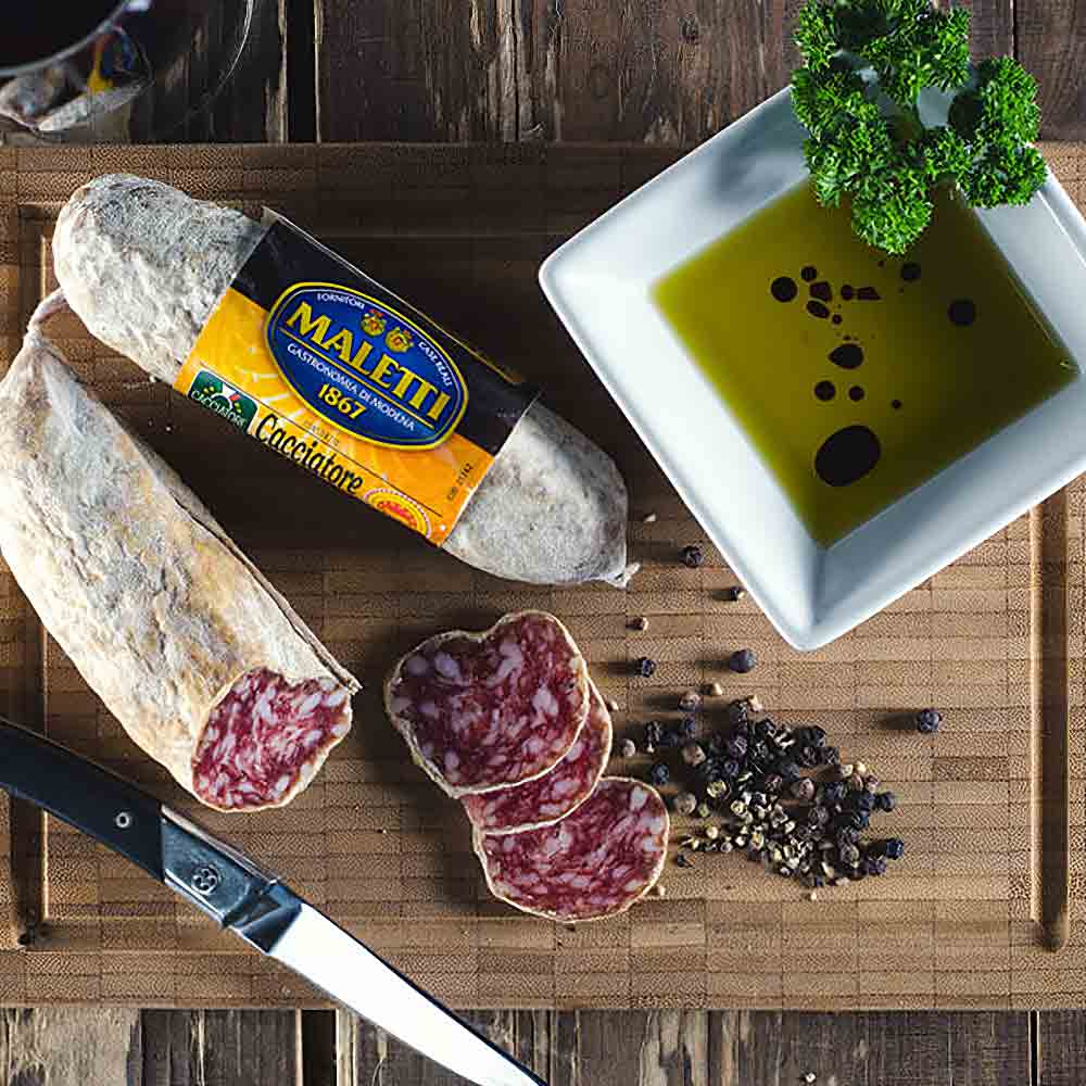 Salami, Olivenöl, Pfeffer, Messer auf Holzbrett, Marke Maletti.