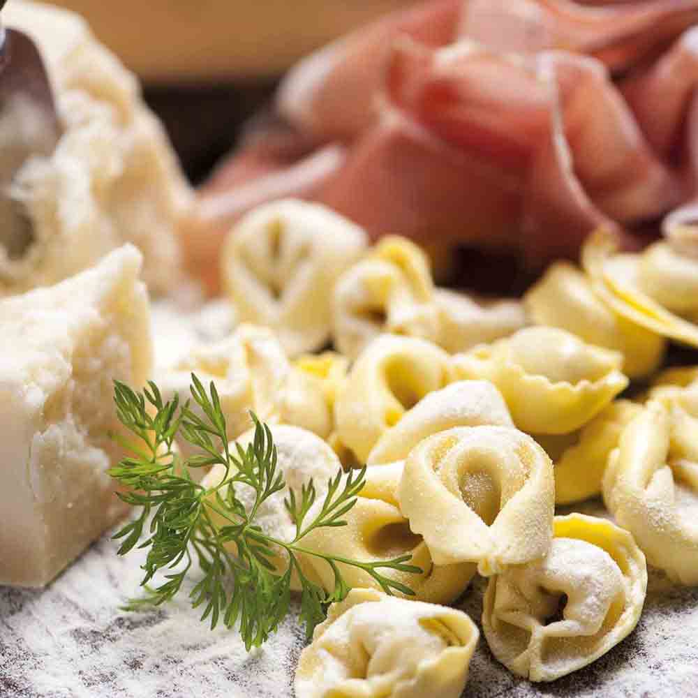 Tortellini, Prosciutto, Parmesan, Kräuter auf Holzbrett, Nahaufnahme.