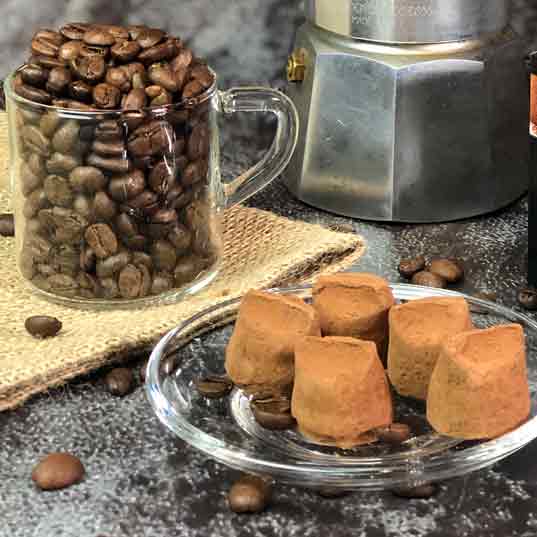 Kaffeebohnen, Mokkakanne, Pralinen auf Tisch mit Jutematte.