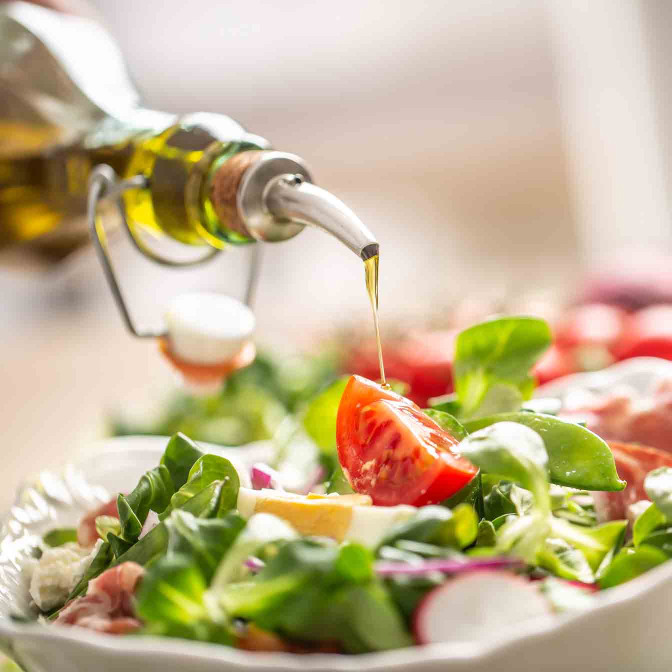 Olivenöl wird über frischen Salat mit Tomaten gegossen.
