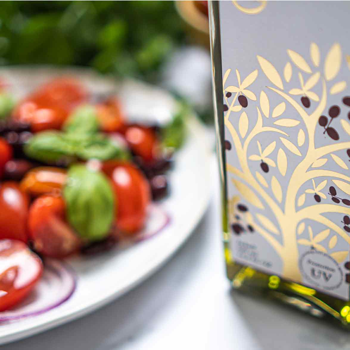 Omed Olivenölflasche vor Teller mit Tomaten und Basilikum.