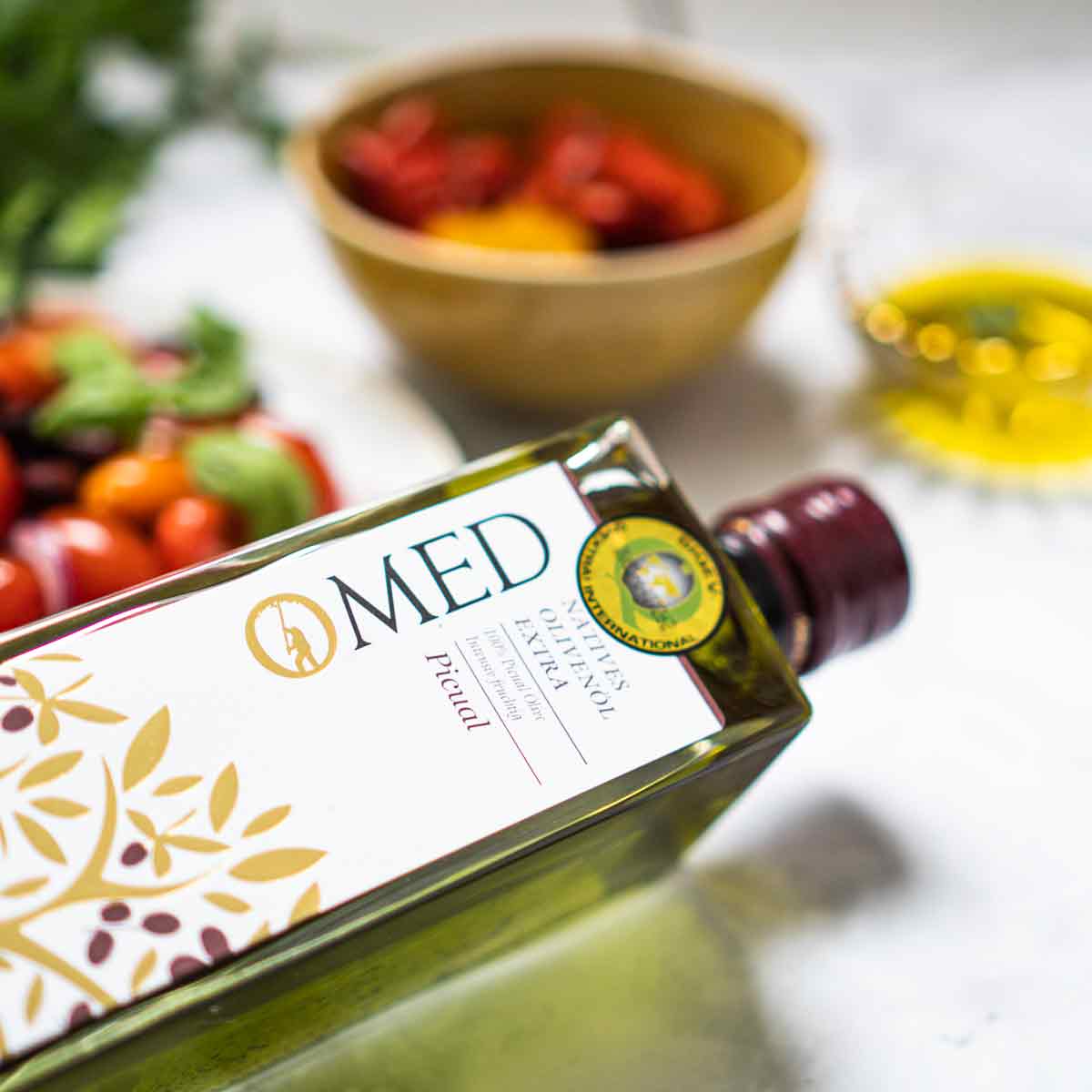 Omed Olivenölflasche mit Schalen im Hintergrund.