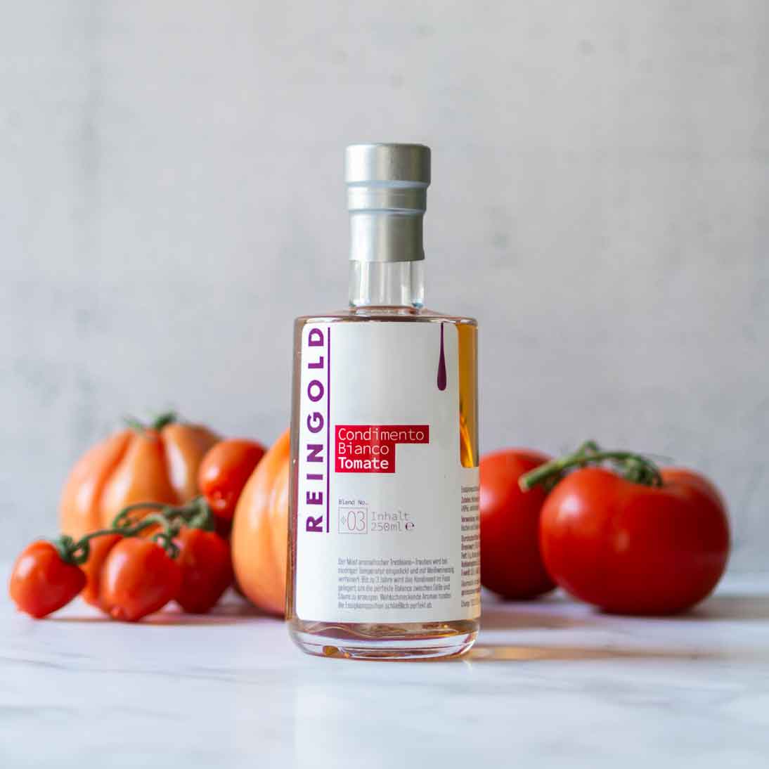 Reingold Tomatenbalsamflasche mit frischen Tomaten im Hintergrund.