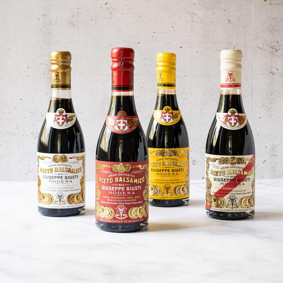Vier Flaschen Aceto Balsamico Giuseppe Giusti vor Betonwand.