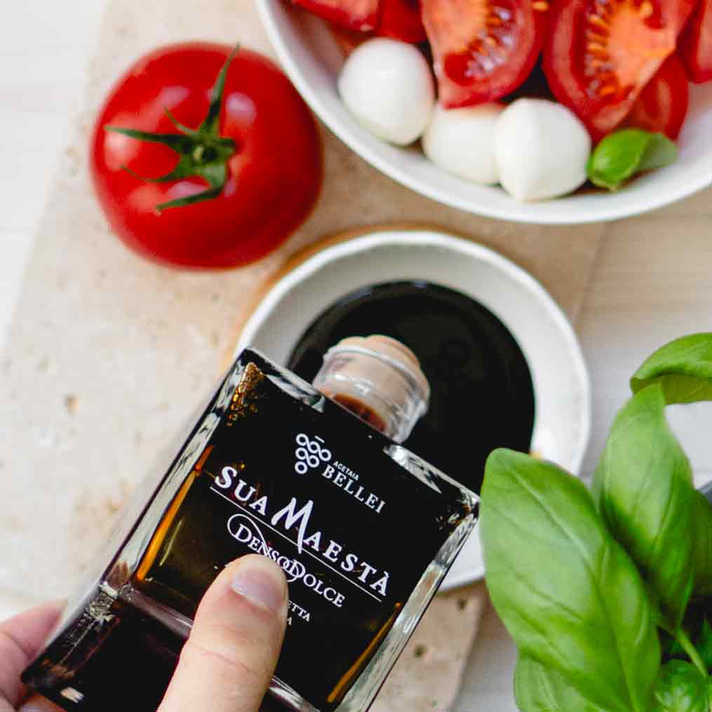 Essigflasche Sua Maestà neben Tomaten und Basilikum.