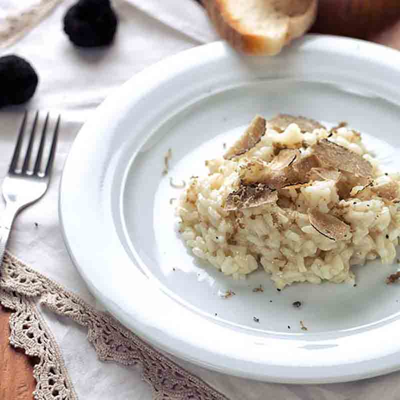 Cremiger Risotto mit gehobeltem Sommertrüffel auf einem weißen Teller, serviert mit Brot und frischen Trüffeln.