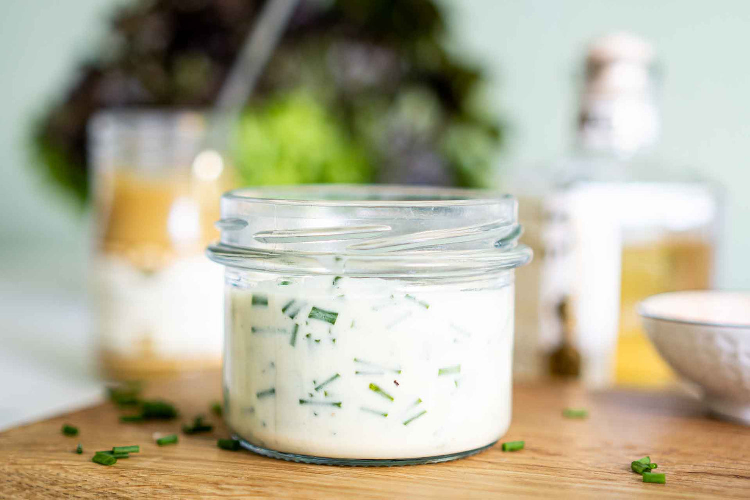 Joghurt-Dressing mit Schnittlauch im Schraubglas. Im Hintergrund stehen Senf und weißer Balsamico
