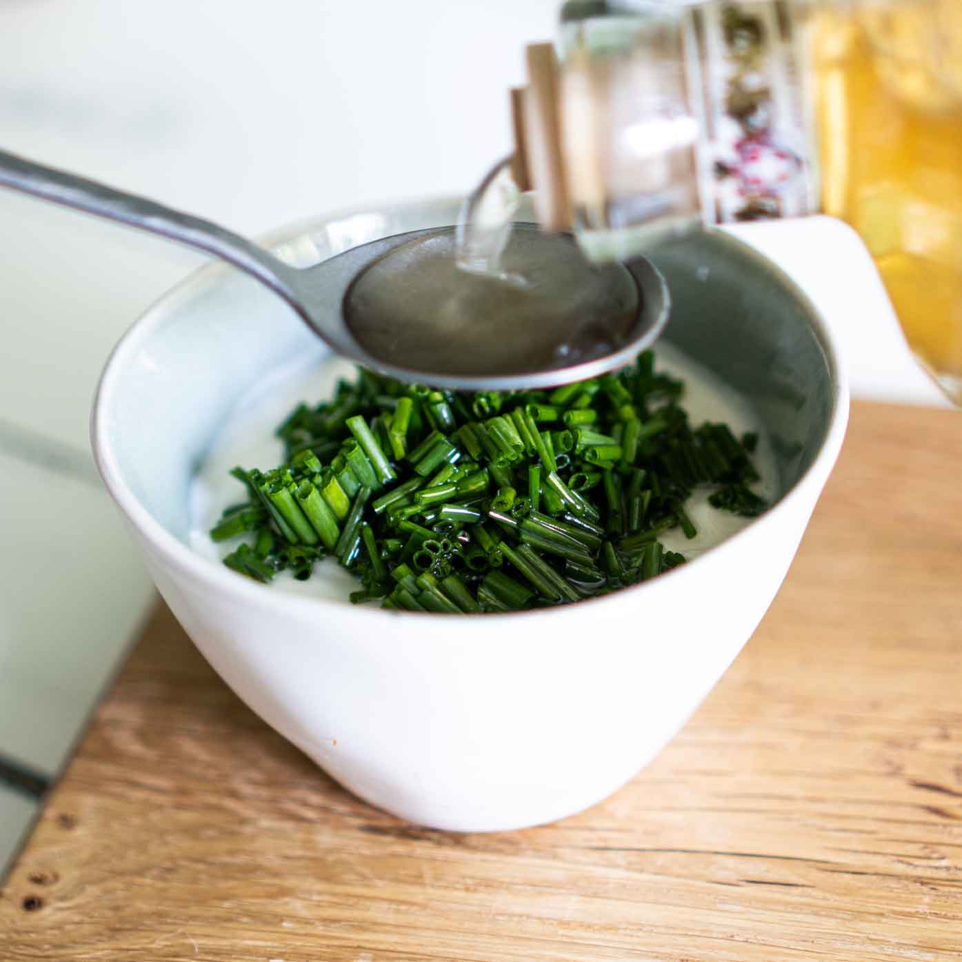 Weißer Balsamessig wird mit einem Esslöffel n das Joghurt-Dressing gegeben.