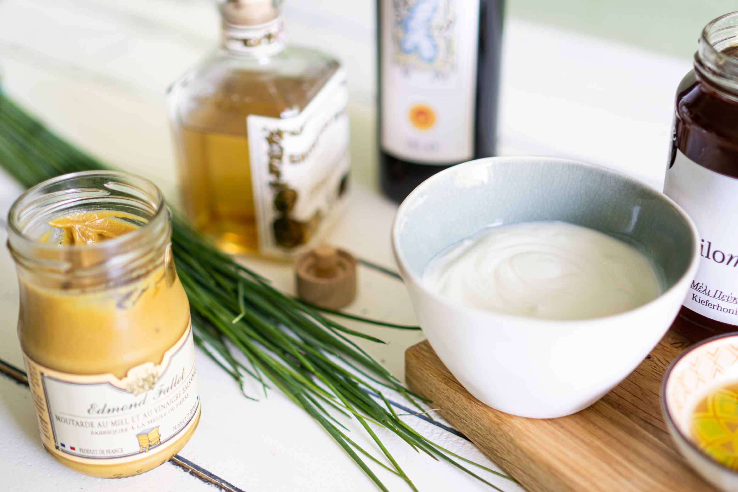 Zutaten für ein Joghurt-Dressing stehen auf einem Tisch. Joghurt, weißer Balsamico, Olivenöl, Honig, Senf, Schnittlauch