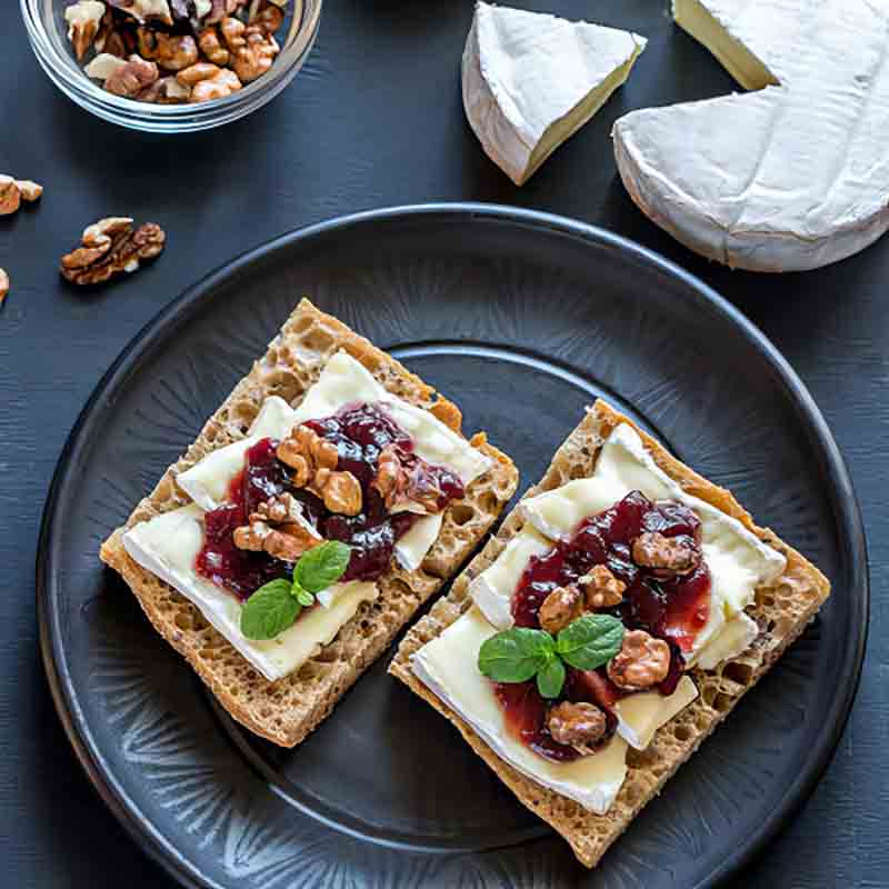 Käsebrot mit Marmelade, Walnüssen und Camembert auf Teller.