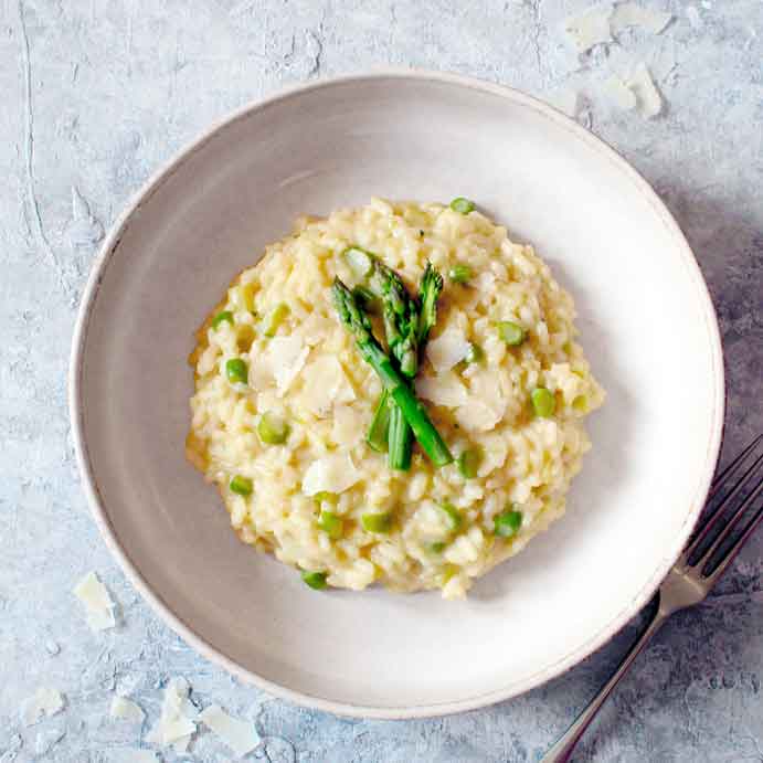 Risotto mit Spargel und Erbsen auf weißem Teller.