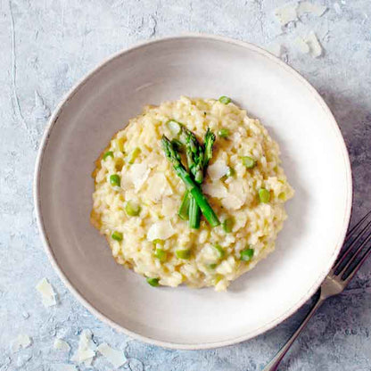 Risotto mit Spargel und Erbsen auf weißem Teller.